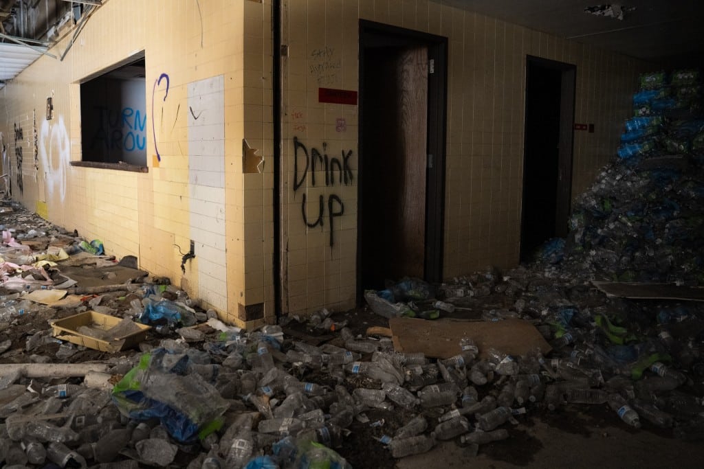 Water bottles piled up in a dark hallway with graffiti on the wall