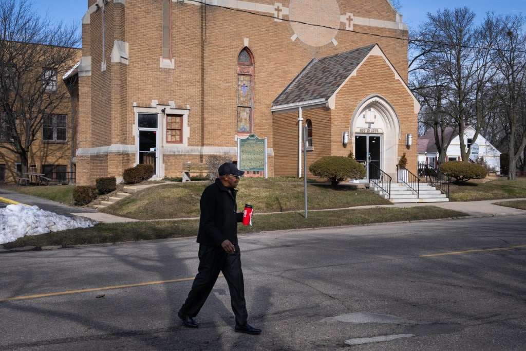 A man holds a cup and walks across the street