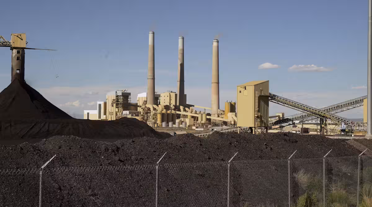 A power plant sits on a hill behind a chain link fence