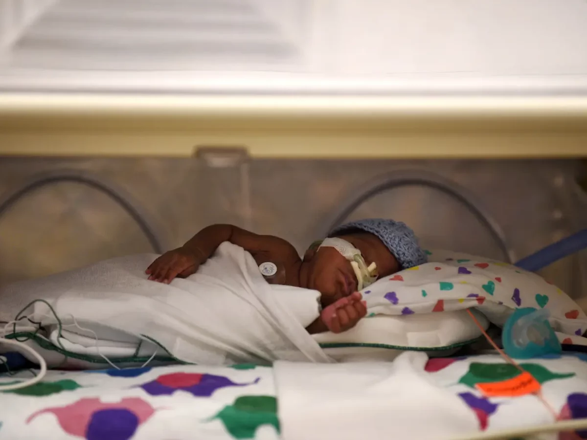 A small baby with tubes in their nose lays in an incubator