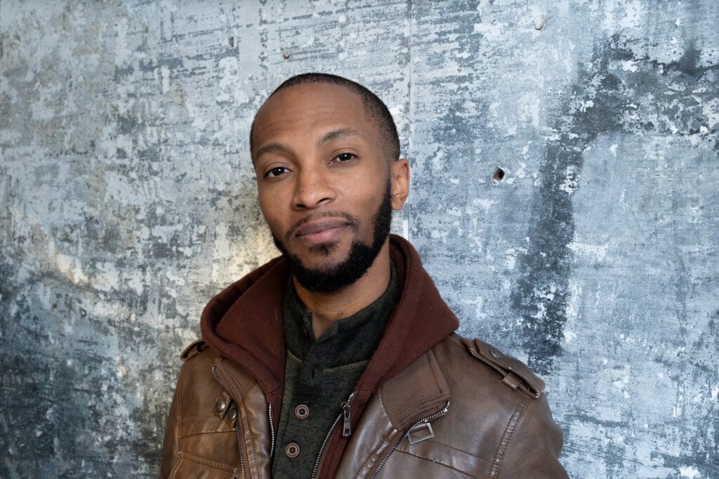 a musician from Detroit poses against a grey textured background