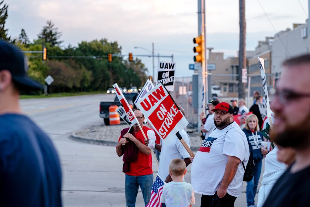 workers line a sidewalk holding picketing signs