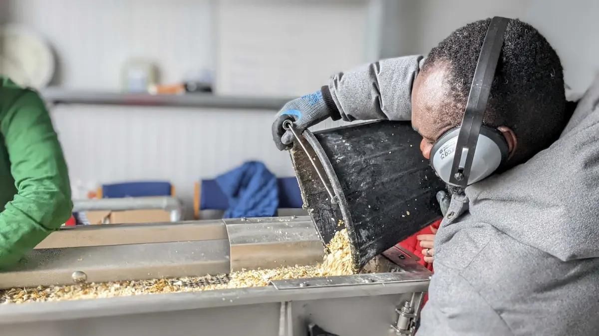 A person pours material from a bucket into a machine.