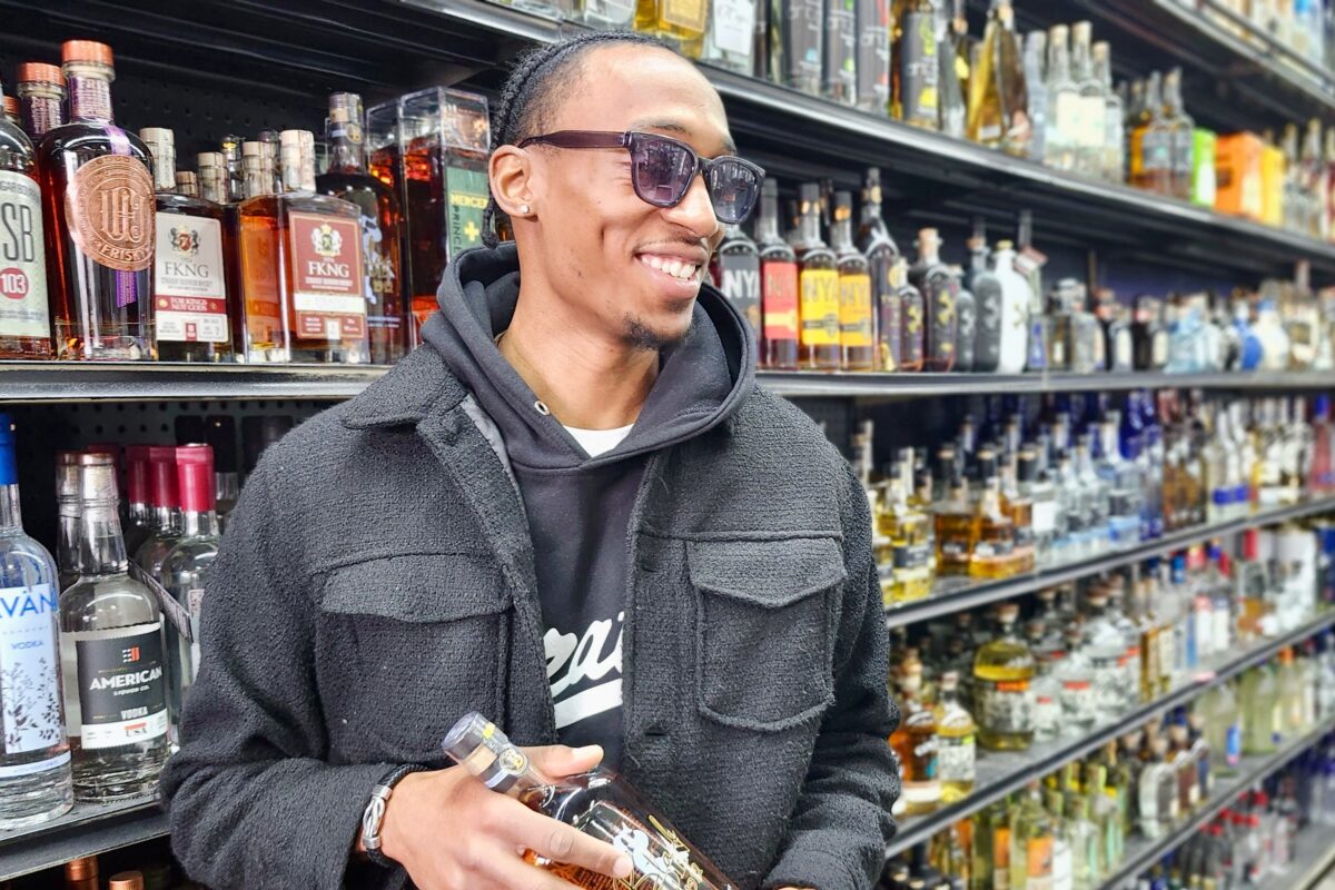 Dominick Lemonious holds a bottle in front of the liquor shelves at his store, the Liquor Basket Gratiot in Detroit.