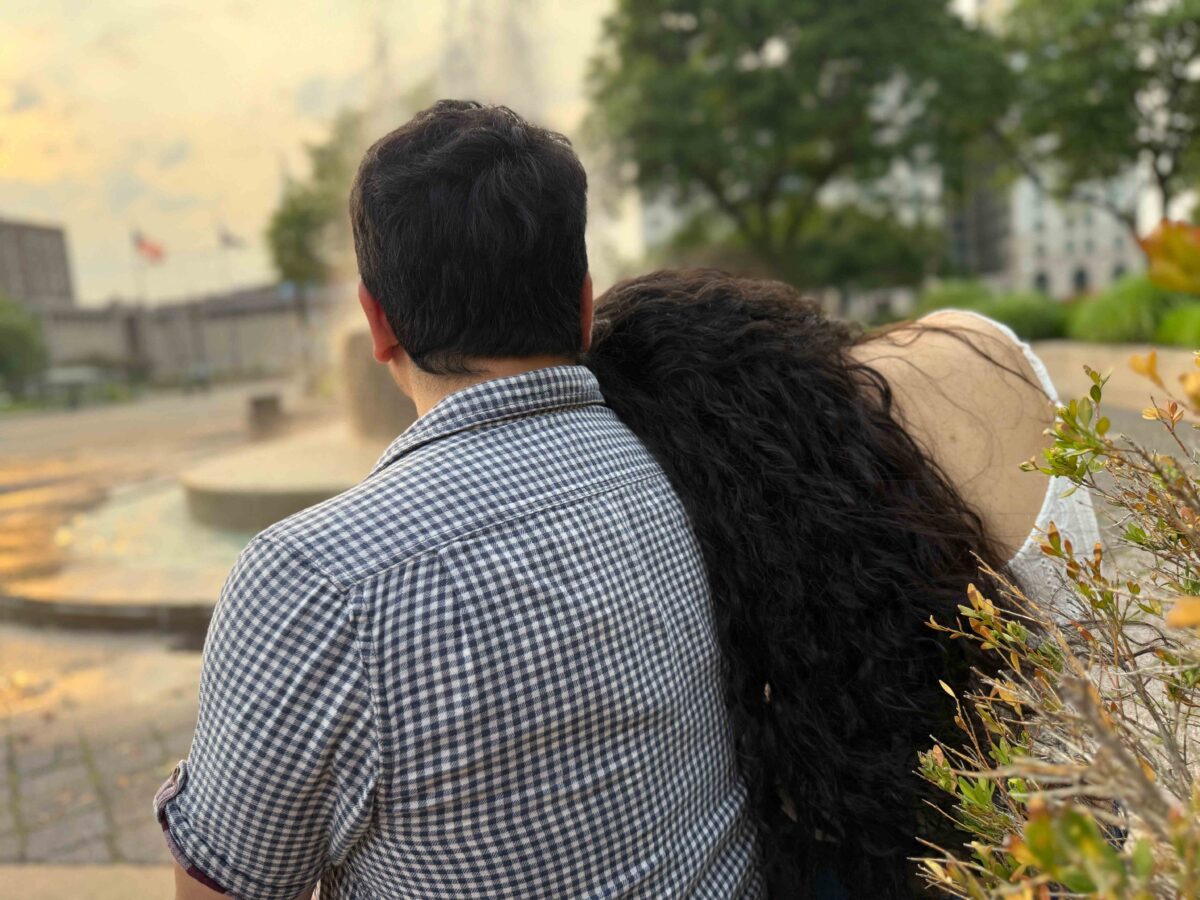 A couple is photographed from behind, with a woman leaning her head on a man's shoulder.