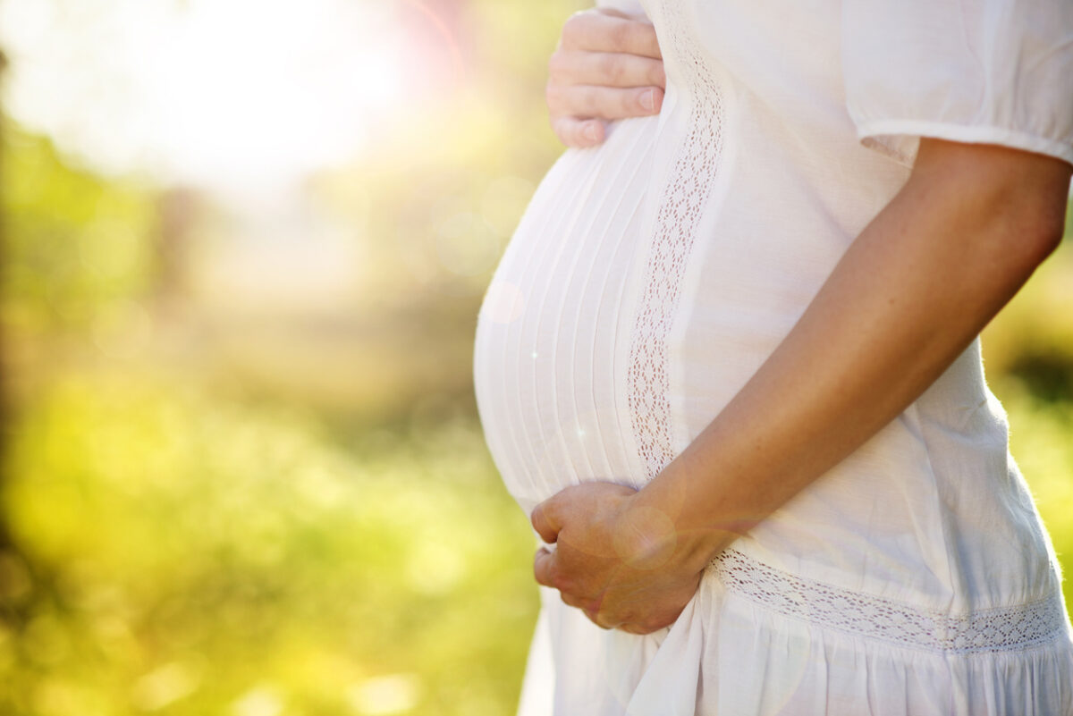 A pregnant person with both hands on their stomach.