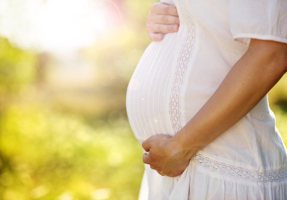 A pregnant person with both hands on their stomach.
