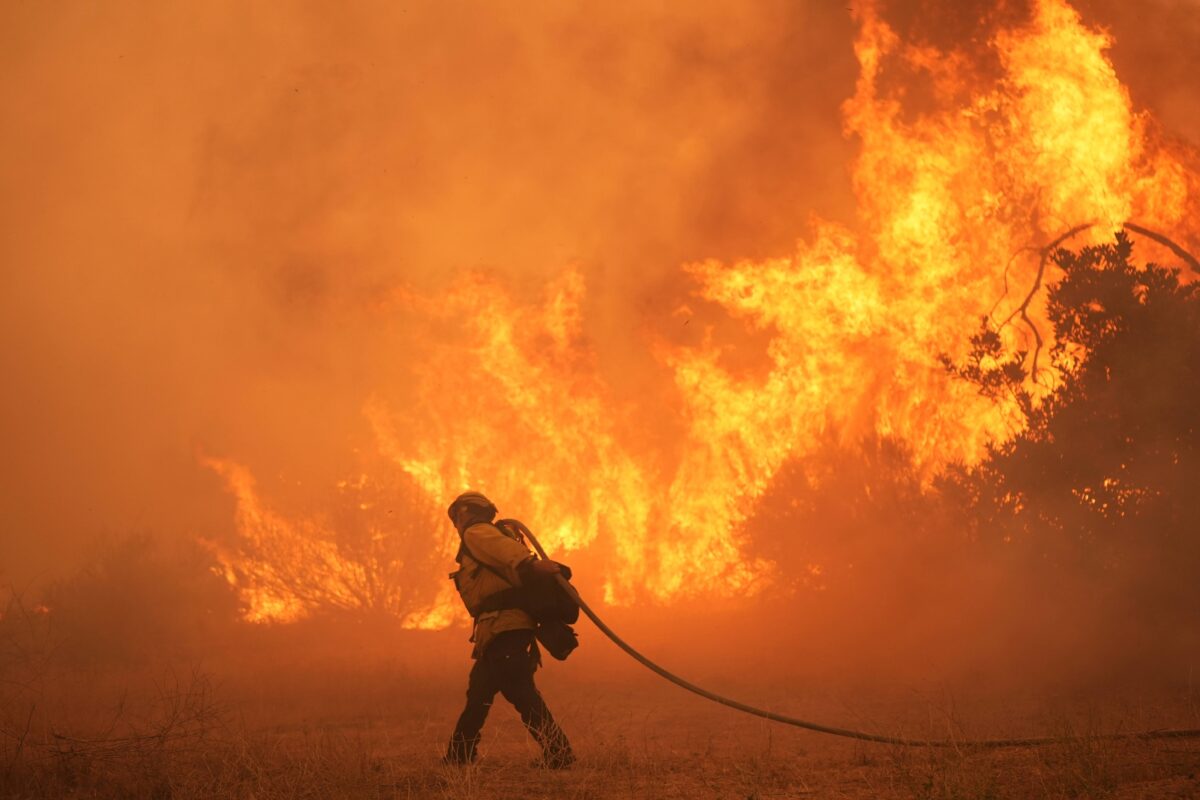 A firefighter drags a hose in front of a wall of flames
