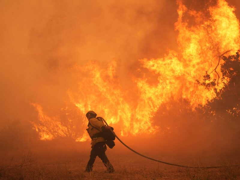 A firefighter drags a hose in front of a wall of flames