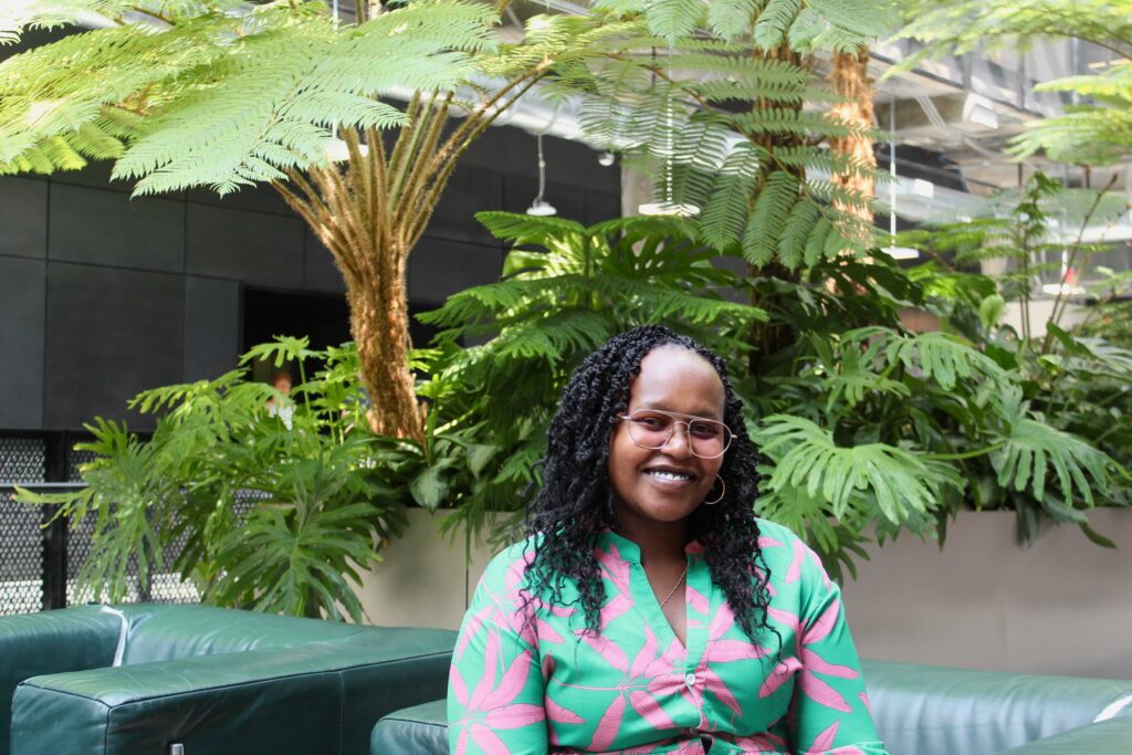 Mary-Jacqueline Muli, founder of The Climate Justice Nurse, sits in front of indoor trees.