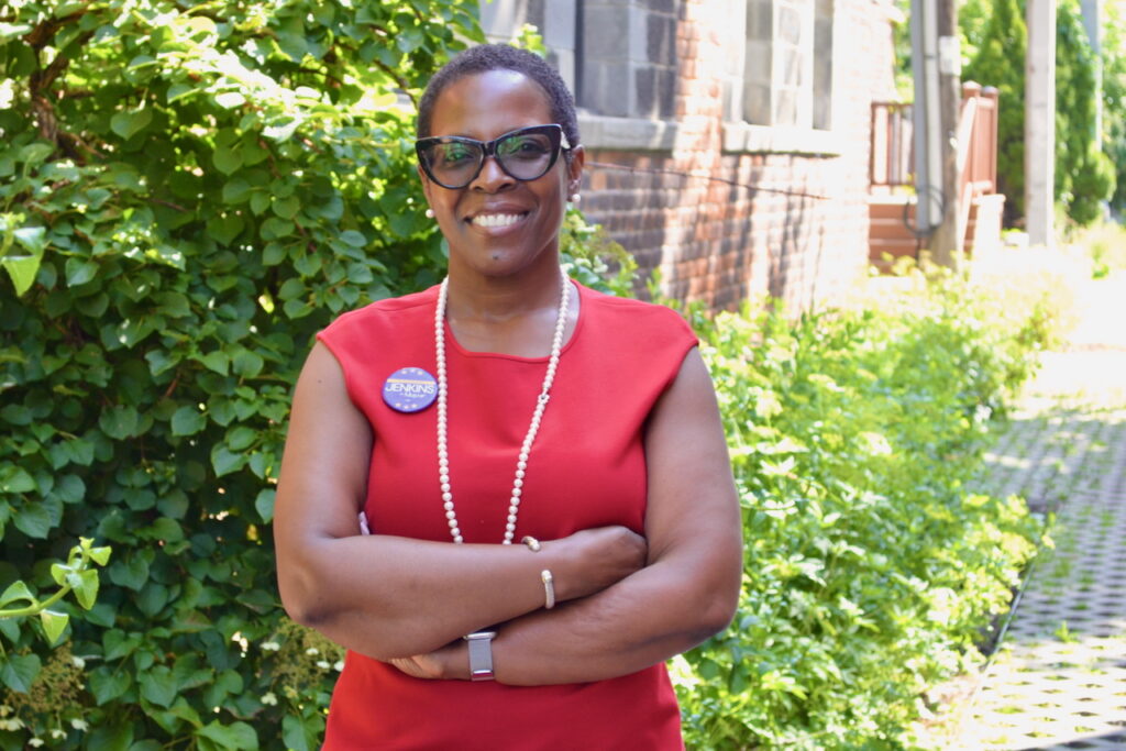 Detroit mayoral candidate Saunteel Jenkins, who is wearing a red shirt, stands with arms crossed.