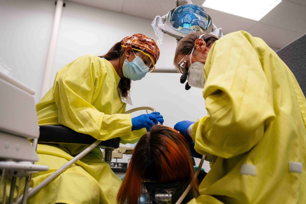 Dr. Gerald Stefan and dental student volunteer Aster Vas, both dressed in yellow dental gowns, fill a cavity at the Malta Clinic.