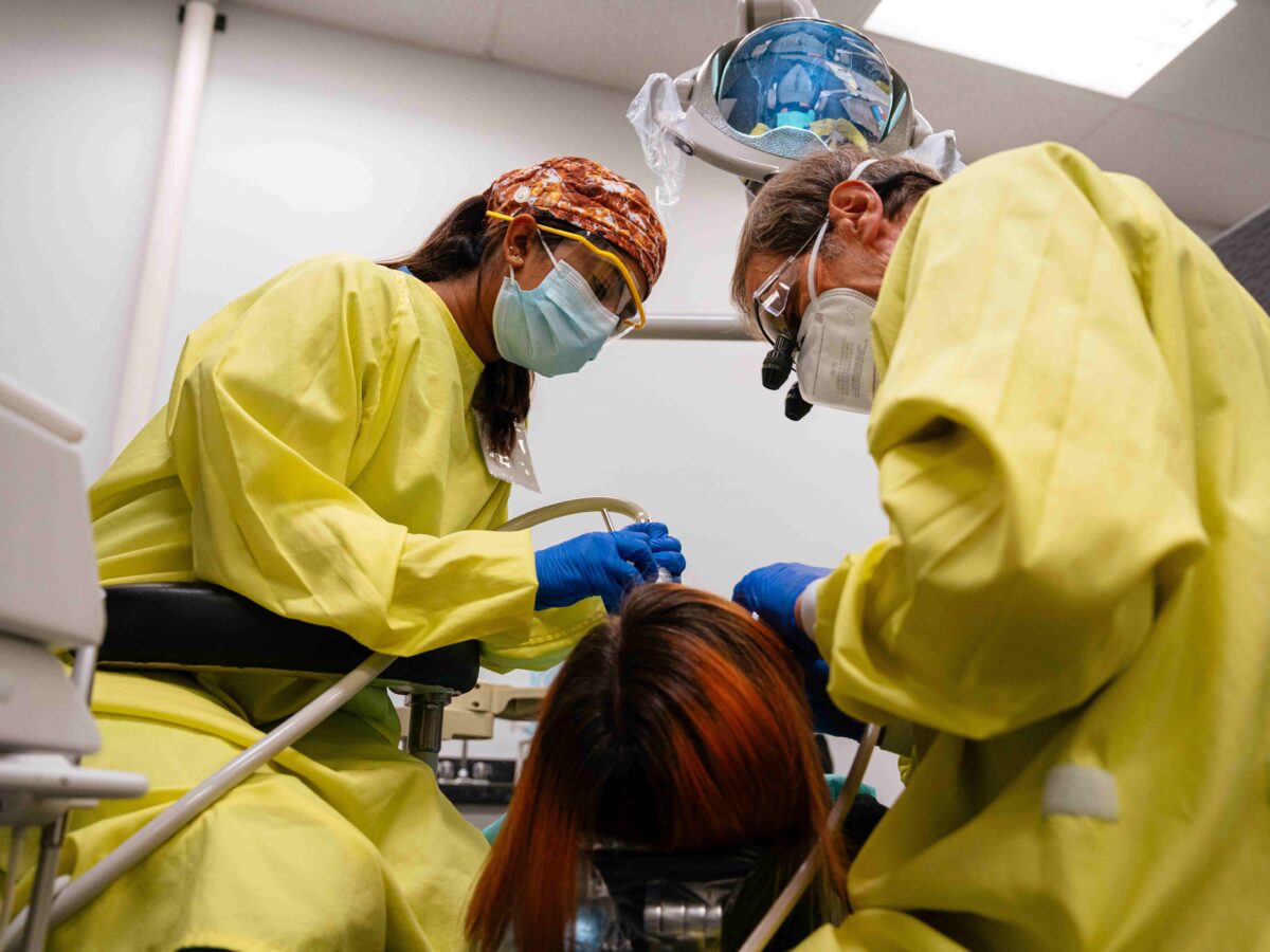 Dr. Gerald Stefan and dental student volunteer Aster Vas, both dressed in yellow dental gowns, fill a cavity at the Malta Clinic.