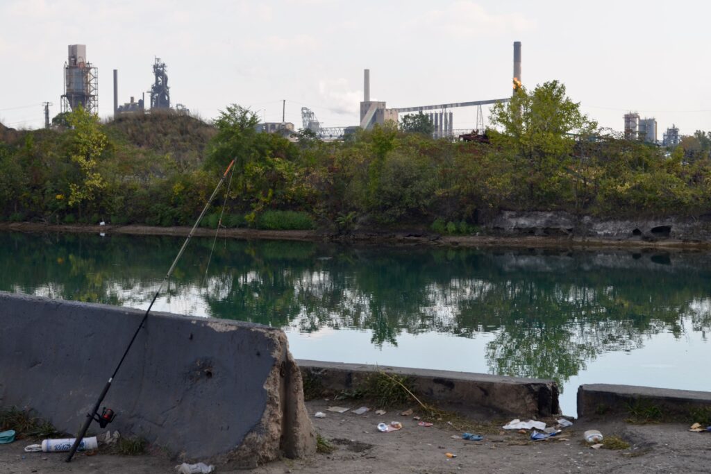 A fishing pole is propped on a concrete block overlooking the Lower Rouge River Old Channel and Zug Island.