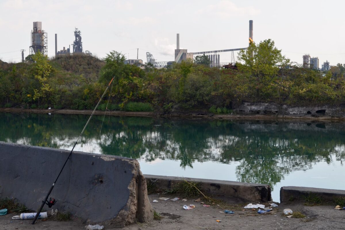 A fishing pole is propped on a concrete block overlooking the Lower Rouge River Old Channel and Zug Island.