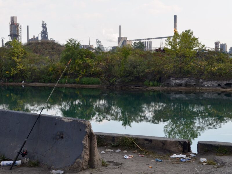 A fishing pole is propped on a concrete block overlooking the Lower Rouge River Old Channel and Zug Island.