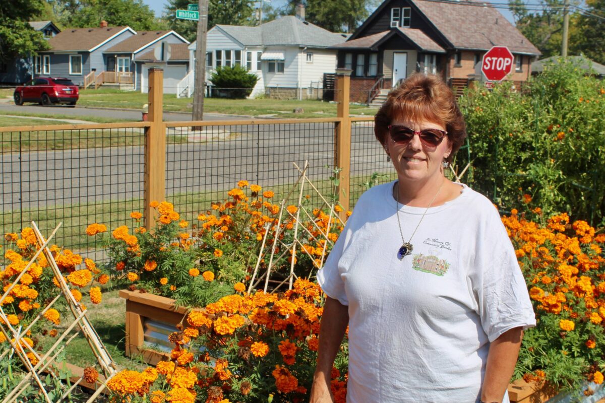 Barb Matney stands in her community garden in front of orange flowers in Detroit's Warrendale neighborhood.