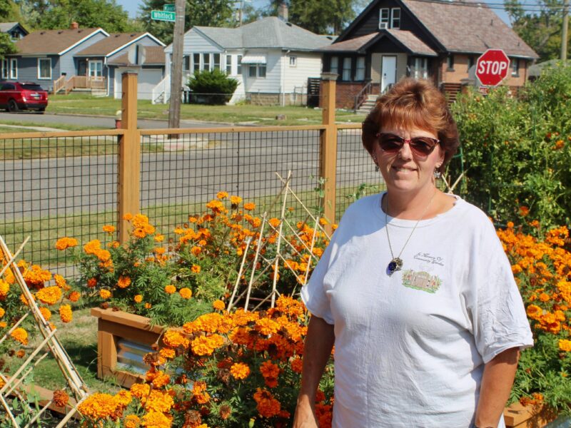 Barb Matney stands in her community garden in front of orange flowers in Detroit's Warrendale neighborhood.