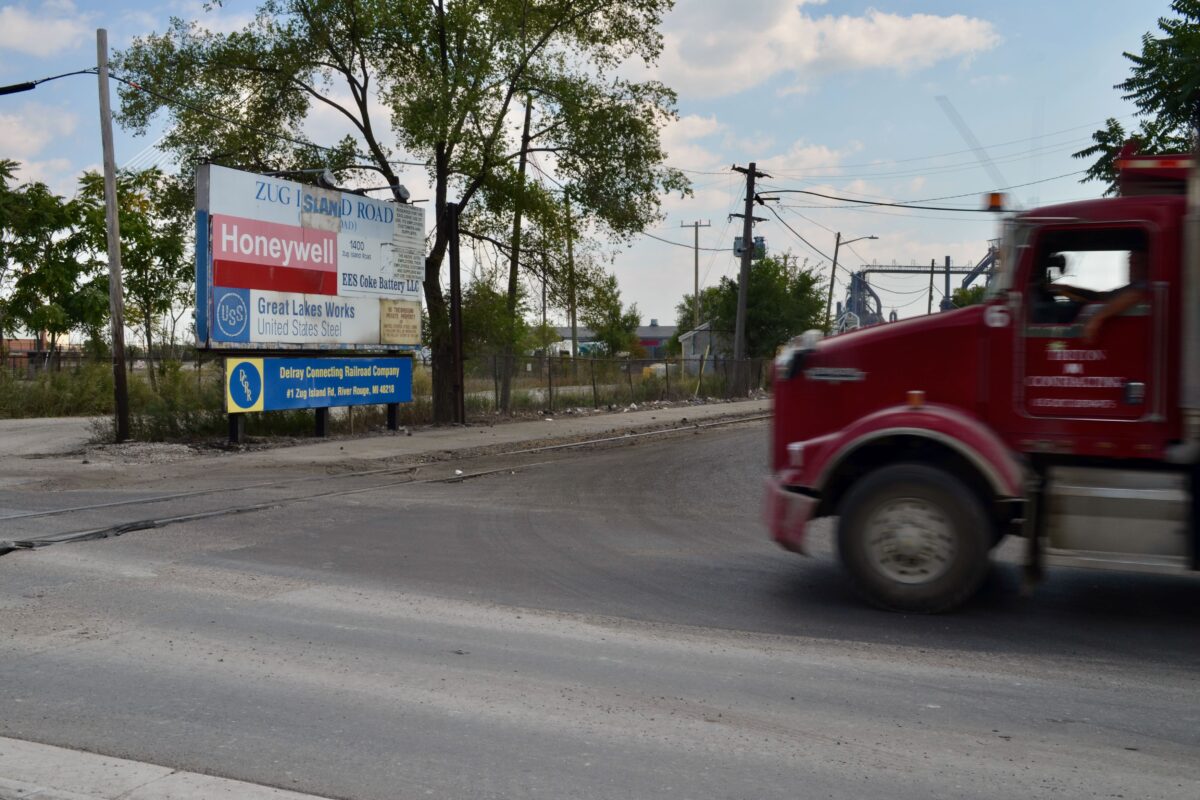 A red truck drives past the Zug Island sign on the corner of West Jefferson Avenue and Zug Island Road.
