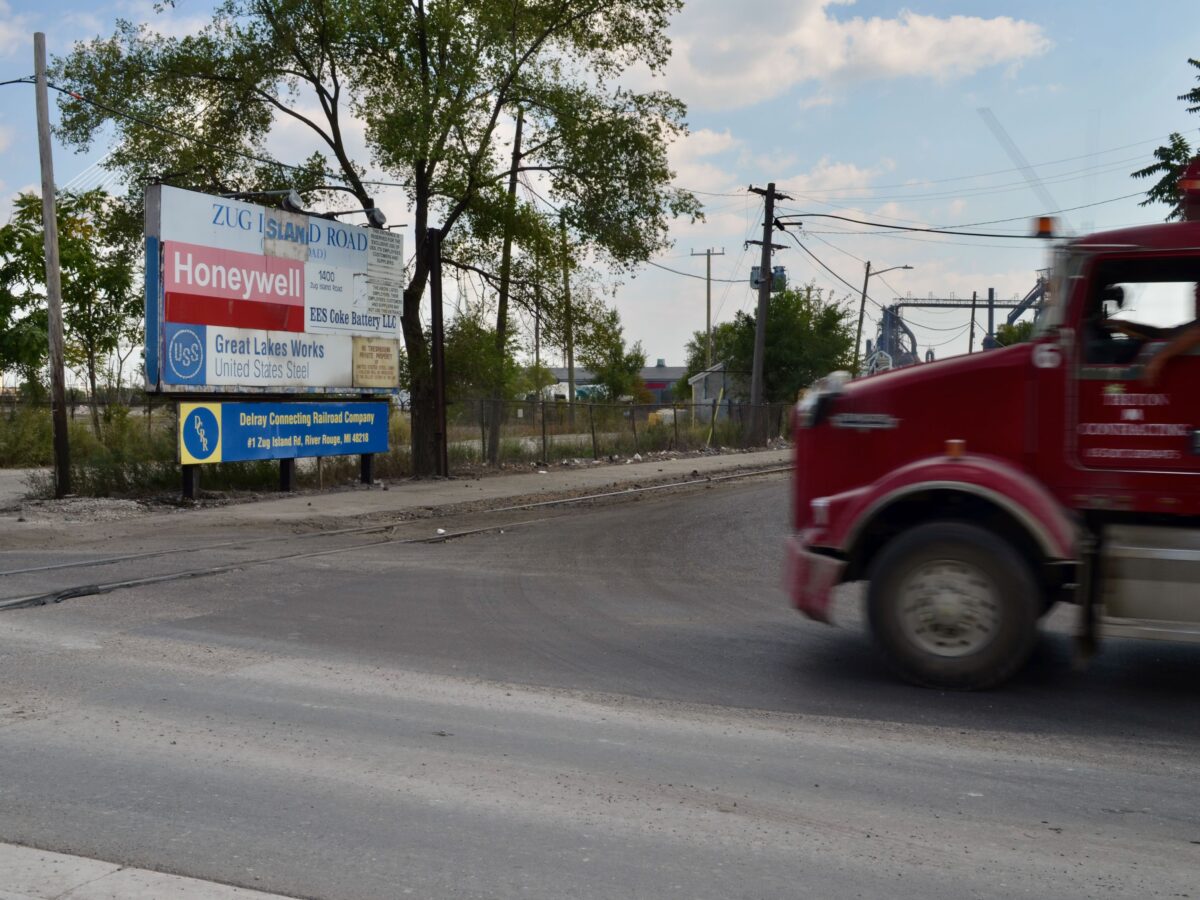 A red truck drives past the Zug Island sign on the corner of West Jefferson Avenue and Zug Island Road.