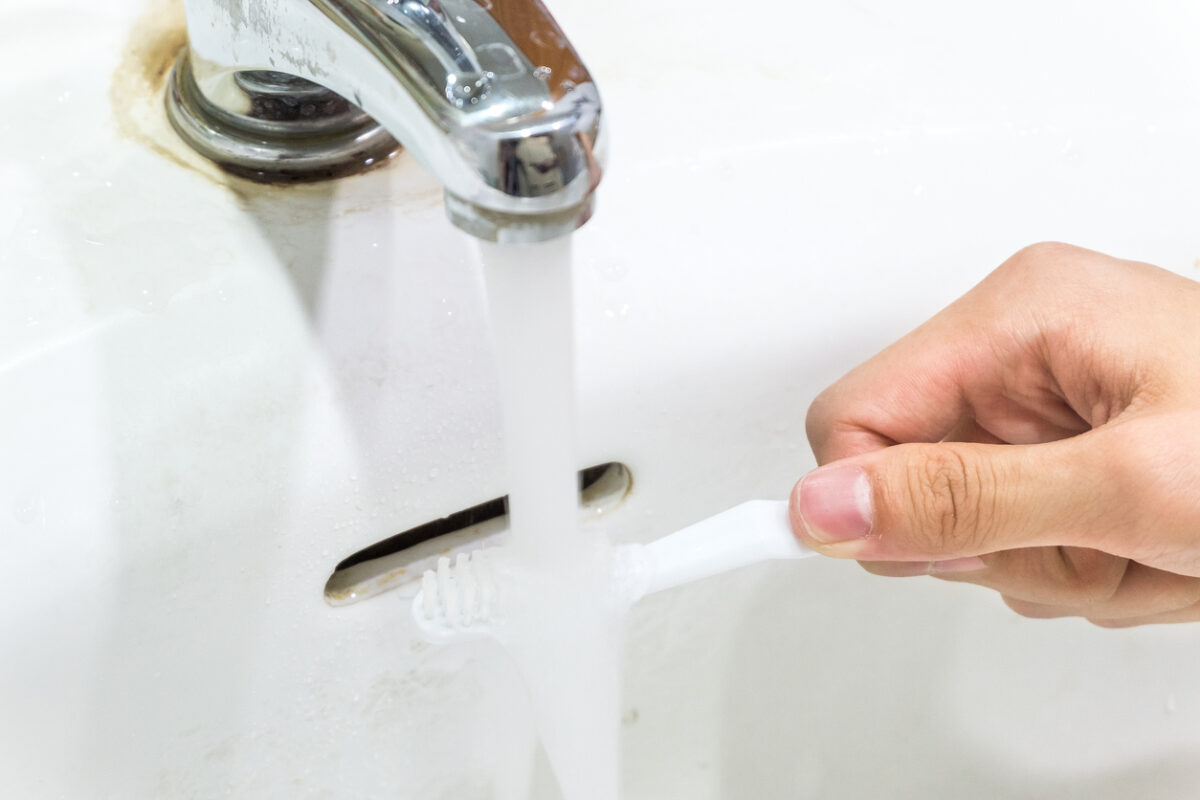A person's hand holds a toothbrush under a running faucet.