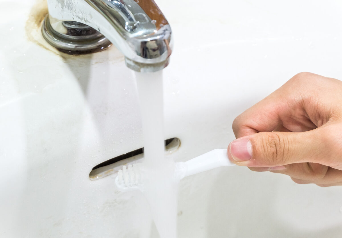 A person's hand holds a toothbrush under a running faucet.
