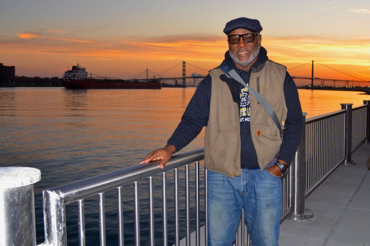 Ralph Wilson, of Lincoln Park, stands on the Detroit Riverwalk with the Ambassador Bridge and Gordie Howe International Bridge behind him at sunset.