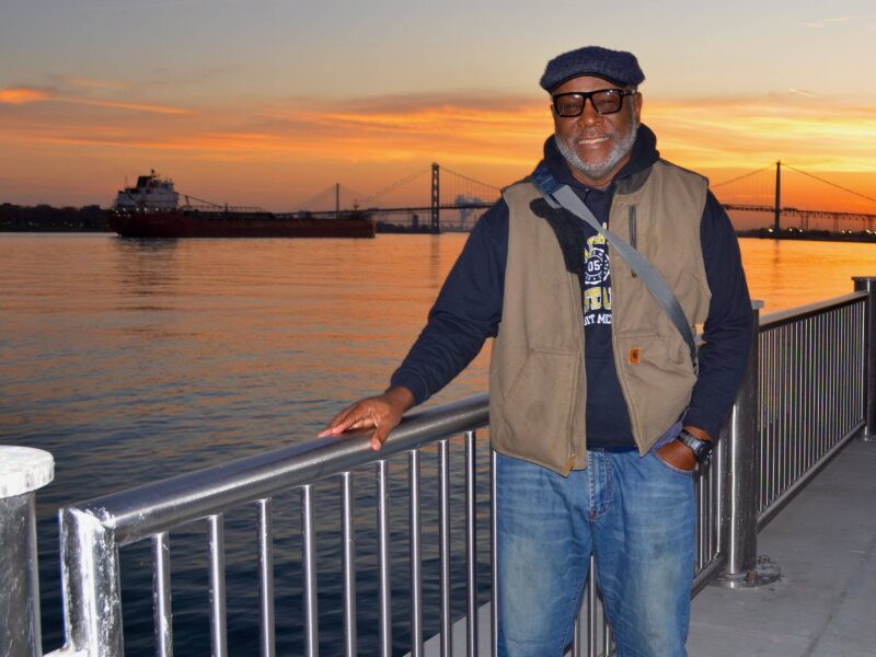 Ralph Wilson, of Lincoln Park, stands on the Detroit Riverwalk with the Ambassador Bridge and Gordie Howe International Bridge behind him at sunset.