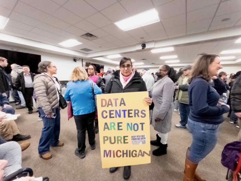 Sadaf Ali holds a sign at Van Buren Township data center meeting: "Data centers are not Pure Michigan."