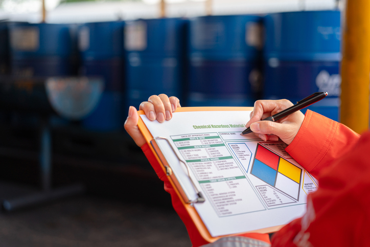 A person wearing orange writes on a hazardous chemical checklist on a clipboard.