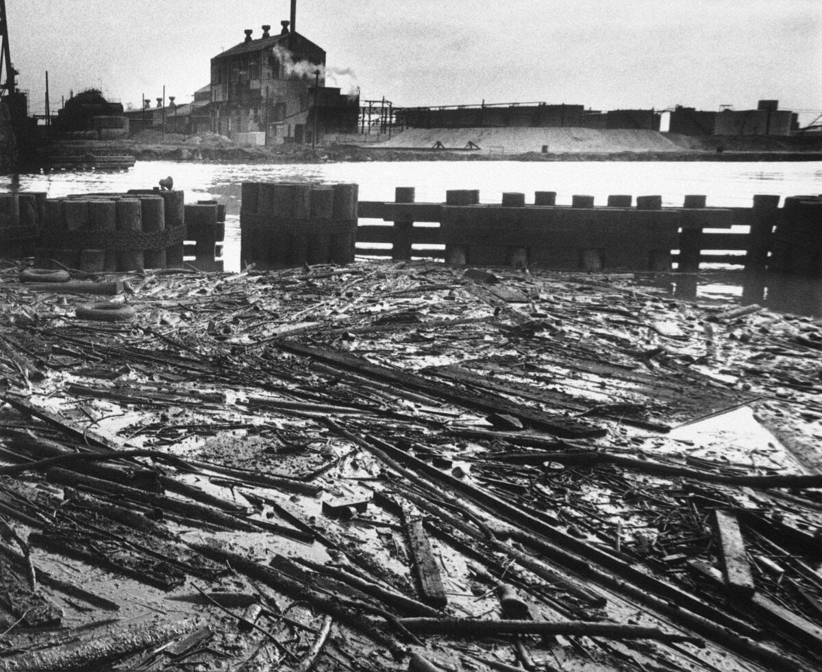 Black-and-white photo of boards, dead fish and other debris lay in an oil slick trapped behind bridge pilings near mouth of Rouge River, May 22, 1969.