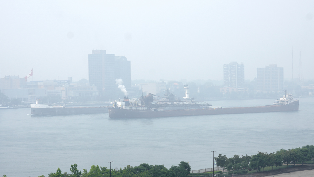 Freighters pass along the Detroit River with Windsor, Ontario in the background as smoke fills the sky reducing visibility Wednesday, June 28, 2023, as seen from Detroit.