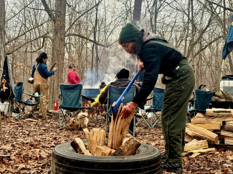 Natalie Perkins, a Black land steward in training at Rouge Park, chops wood for the fire.