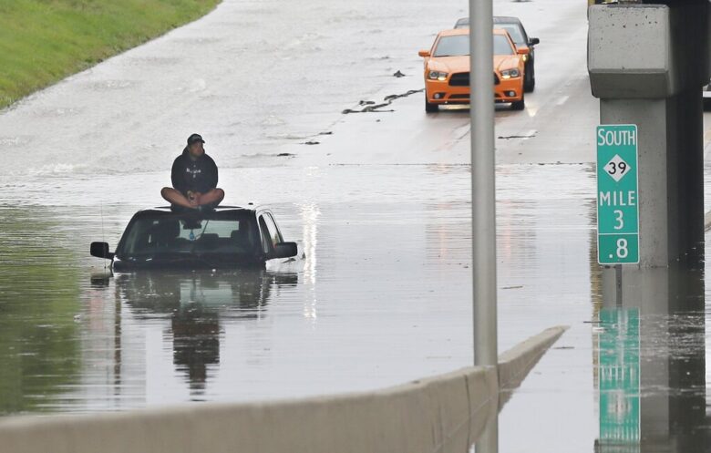 A stranded motorist sits on top his car as he awaits rescue from the flooded Southfield Freeway.