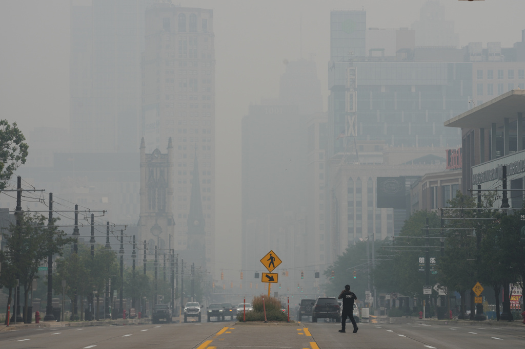 A pedestrian crosses the street as the Detroit city skyline is obscured during poor air quality due to smoke from Canadian wildfires